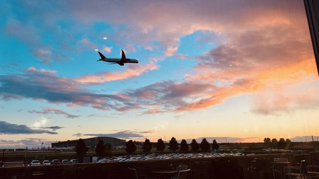 Plane taking off over London Heathrow Terminal 5. There's a sunset in the background.