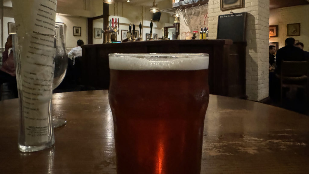 A pint of beer on a table in a pub with a view of the bar in the background