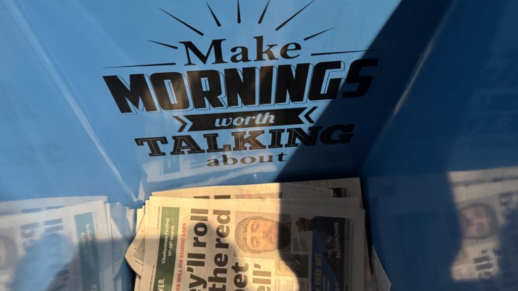 The image shows a blue Metro newspaper container with a motivational phrase printed on it that reads "Make MORNINGS worth TALKING about" in a bold, stylized typography. The word "MORNINGS" is particularly prominent and appears to be in capital letters.