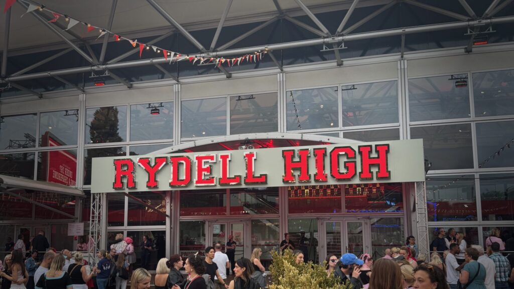 Exterior view of the Rydell High building entrance with crowds of visitors gathered outside under bunting decorations