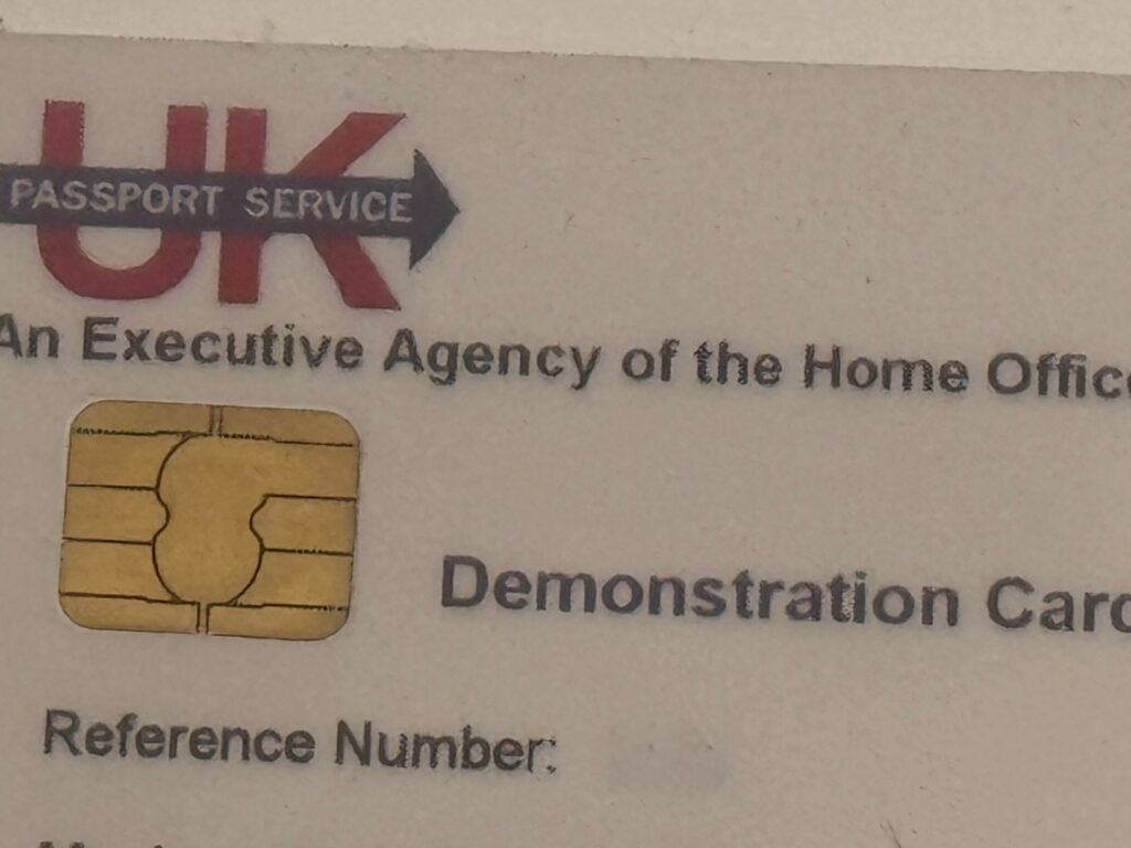 A close-up photograph of a worn card showing the UK Passport Service logo in red with an arrow, text reading "An Executive Agency of the Home Office", a gold EMV chip, and the words "Demonstration Card" and "Reference Number:" printed below