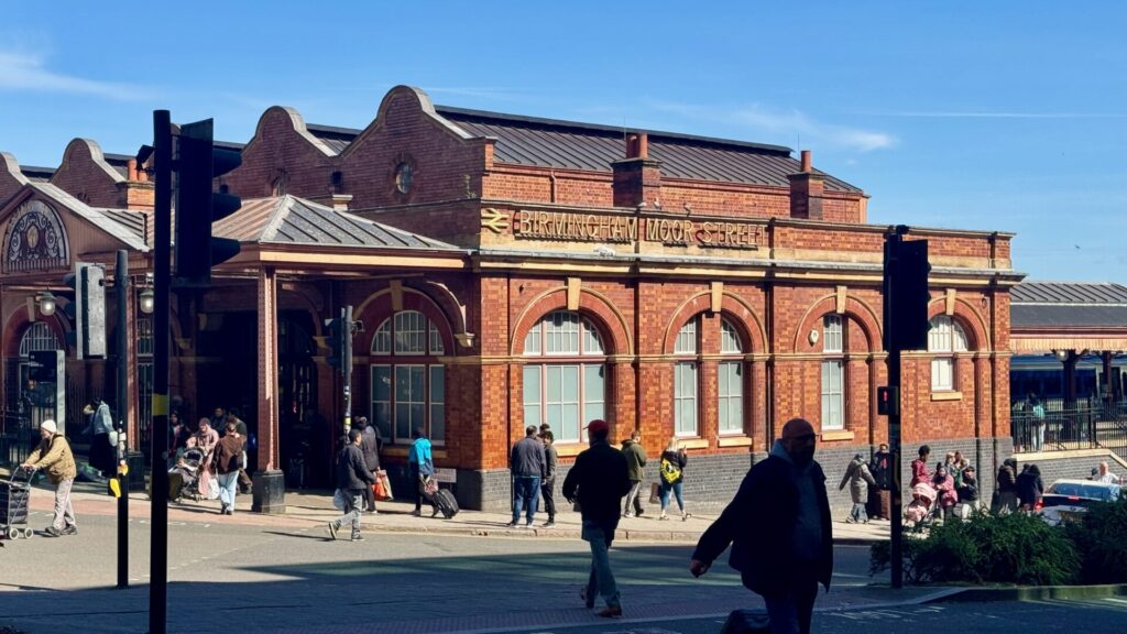 Birmingham Moor Street railway station, a red-brick building with arched windows and period details, seen on a bright day with people walking past and gathering near the entrance; the station served as a key part of Easter weekend travel.