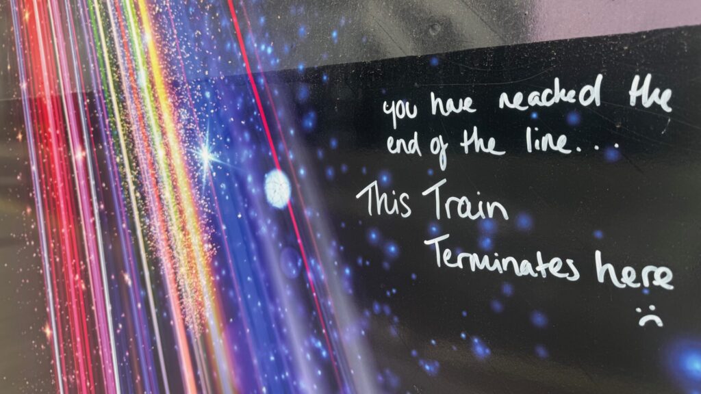 Graffiti handwritten in white marker on the dark background of a Starlight Express show sign at Wembley Park. The text reads: "you have reached the end of the line… This Train Terminates here". To the left, the original sign features colourful beams of light streaking diagonally against a deep blue, star-filled cosmic backdrop.