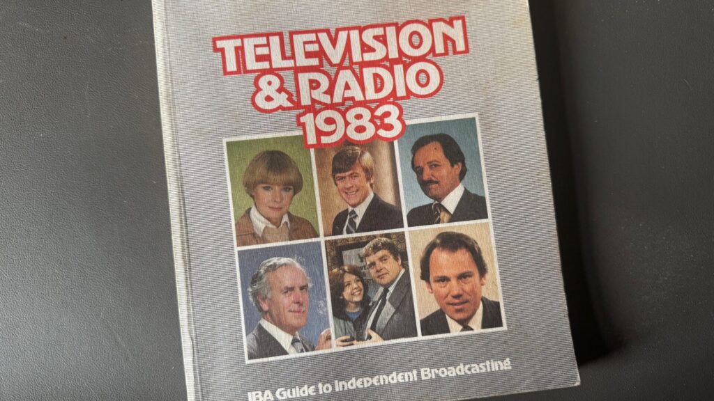 A hardback book photographed on a dark surface. The cover reads "Television & Radio 1983" in large red and white bold lettering, with the subtitle "IBA Guide to Independent Broadcasting" along the bottom. The cover features a grid of six colour photographs of television personalities — three men and one woman in formal attire in the top row, and three further individuals, including a man and woman pictured together, in the bottom row. The styling and photography are typical of the early 1980s.