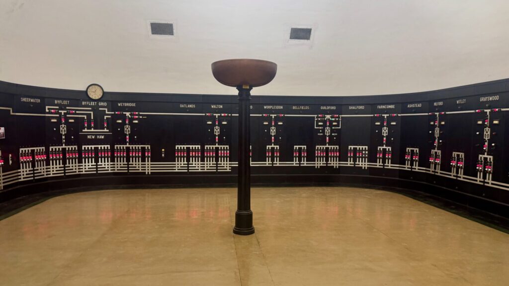 Interior of the 1936 Southern Railway electrical control room at Woking, with illuminated railway power diagrams around the curved walls and a large Art Deco uplighter beneath the domed ceiling.