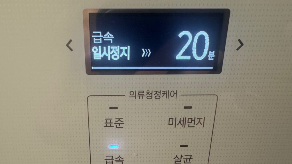 Close-up of a Korean clothes-care appliance in a Seoul hotel room. Its illuminated display shows the rapid programme paused, with 20 minutes indicated and four cleaning modes labelled in Korean.